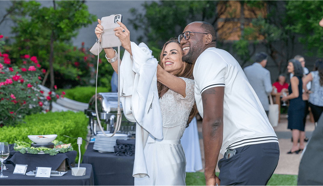 Darryll Stinson smiling while taking a picture with an event attendee or fan at an outdoor professional networking or media reception.